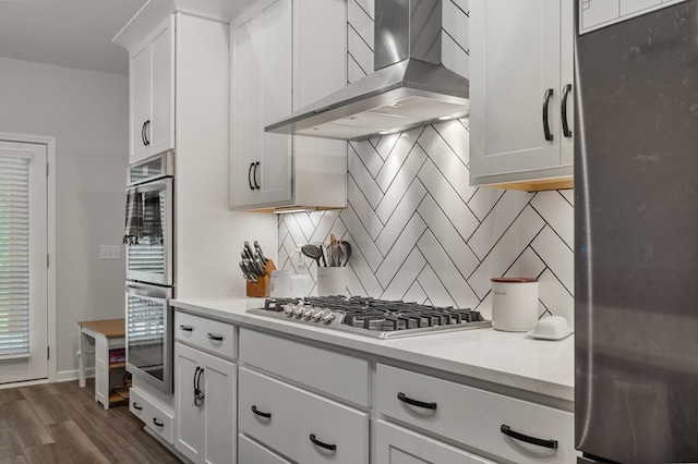 kitchen with backsplash, dark wood-type flooring, wall chimney exhaust hood, appliances with stainless steel finishes, and white cabinetry