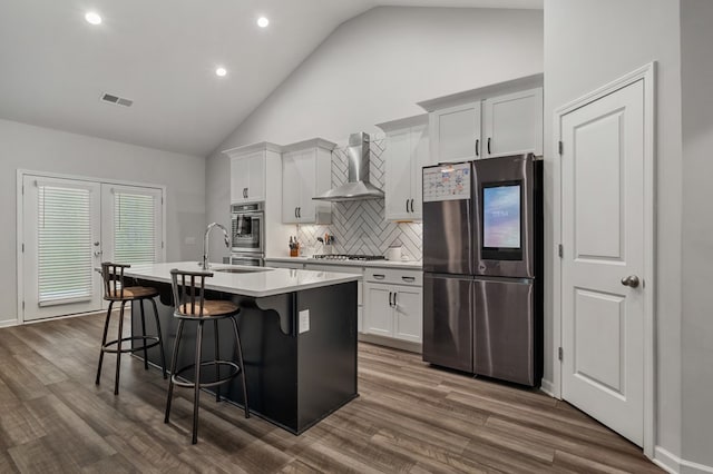 kitchen with wall chimney range hood, dark hardwood / wood-style floors, an island with sink, white cabinetry, and stainless steel appliances