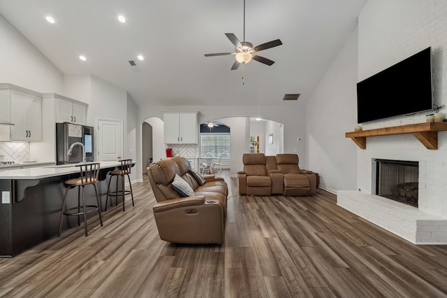 living room featuring ceiling fan, sink, high vaulted ceiling, light hardwood / wood-style flooring, and a fireplace