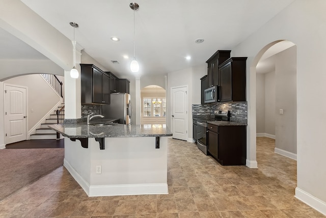 kitchen featuring sink, dark stone countertops, stainless steel appliances, decorative light fixtures, and kitchen peninsula