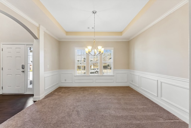 unfurnished dining area featuring an inviting chandelier, a raised ceiling, and dark colored carpet