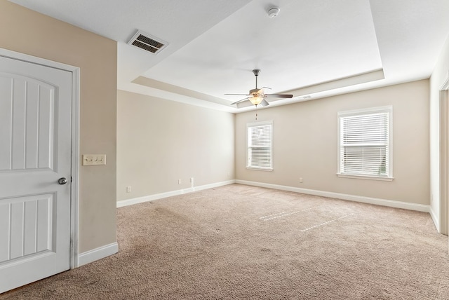 empty room with light carpet, a raised ceiling, and ceiling fan