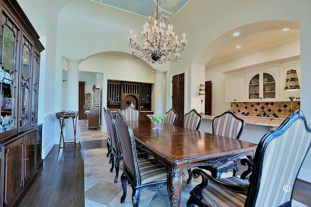 dining area featuring hardwood / wood-style floors, a towering ceiling, decorative columns, and an inviting chandelier