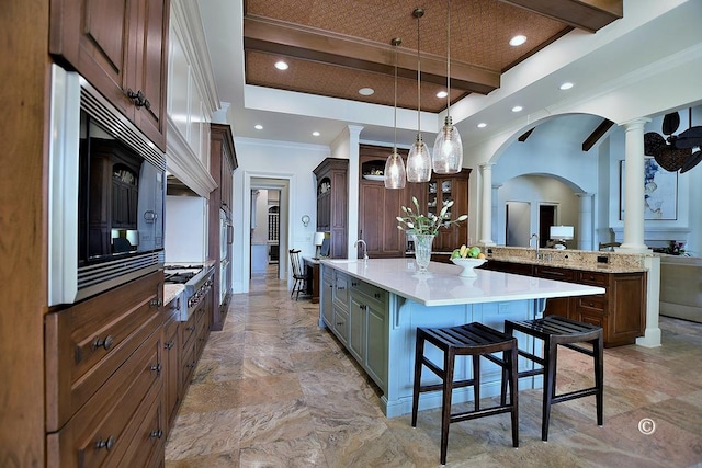 kitchen with black microwave, a kitchen breakfast bar, decorative columns, a large island with sink, and decorative light fixtures