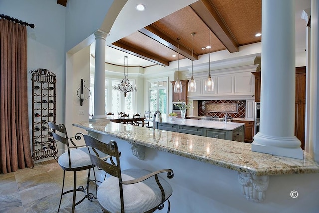 kitchen featuring decorative light fixtures, beam ceiling, light stone counters, and kitchen peninsula