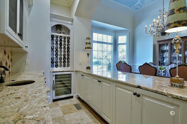 kitchen featuring white cabinets, sink, decorative light fixtures, light stone counters, and beverage cooler