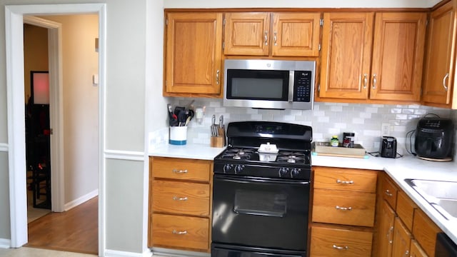 kitchen with light hardwood / wood-style floors, backsplash, black appliances, and sink