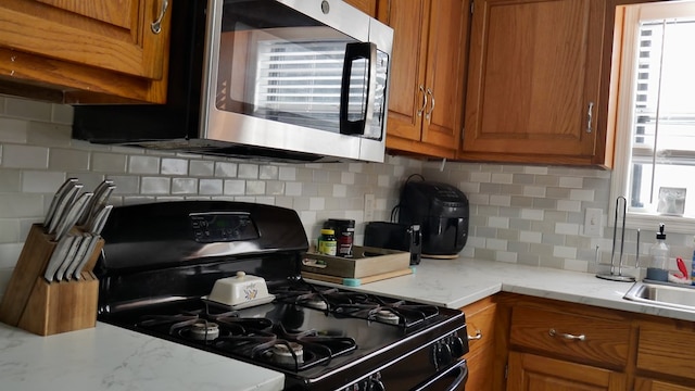 kitchen featuring black gas stove, sink, light stone counters, and decorative backsplash