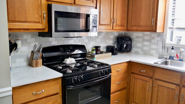 kitchen with black gas range, sink, backsplash, and light stone countertops