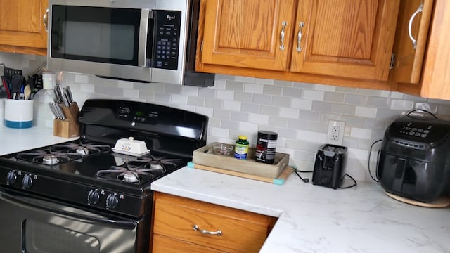 kitchen featuring black gas range oven, tasteful backsplash, and light stone countertops