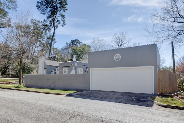 view of front of house featuring driveway, a chimney, fence, and stucco siding