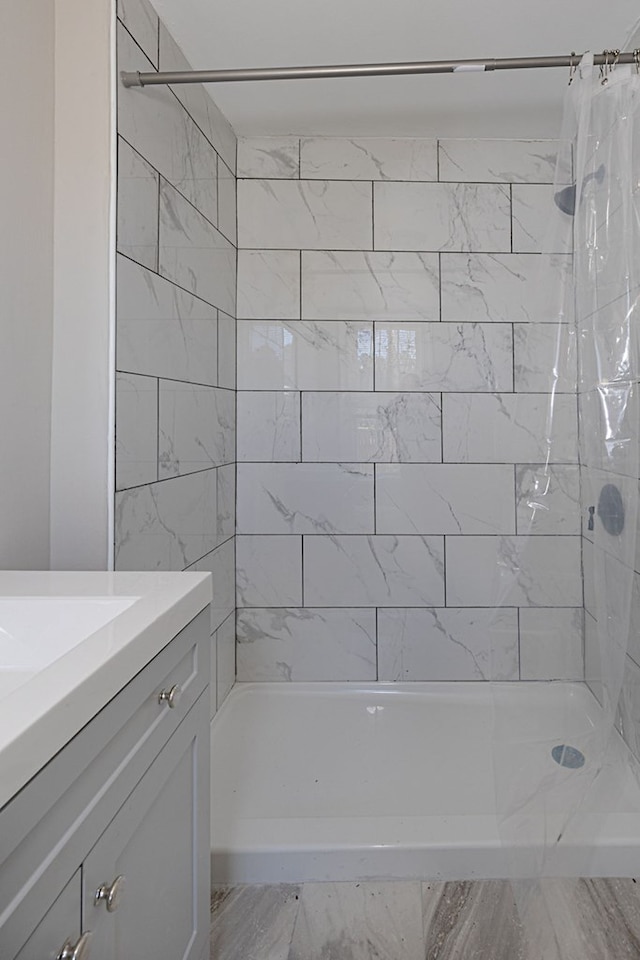 full bath featuring marble finish floor, tiled shower, and vanity