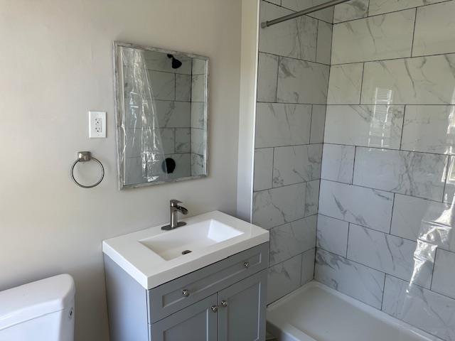 full bathroom featuring toilet, tiled shower, and vanity