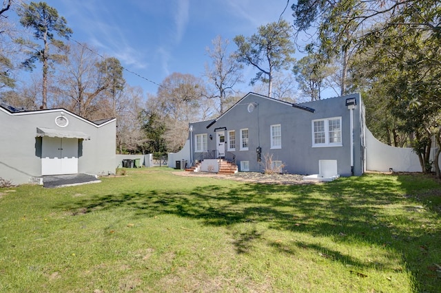 rear view of property with a lawn, fence, central AC unit, and stucco siding