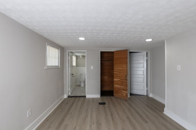 unfurnished bedroom with ensuite bathroom, light wood-style flooring, baseboards, and a textured ceiling