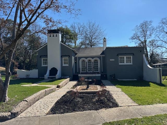 view of front of home with a front yard, a chimney, and stucco siding