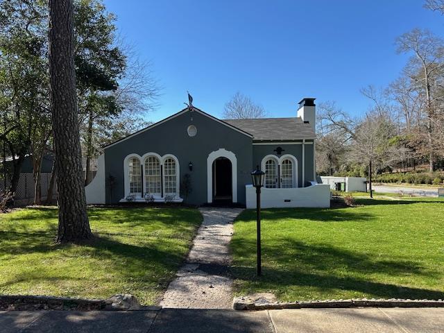 view of front of property featuring a front lawn, a chimney, and stucco siding