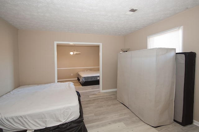 bedroom featuring a textured ceiling, light hardwood / wood-style flooring, and an inviting chandelier