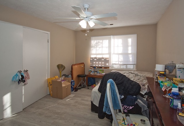 bedroom with light wood-type flooring, ceiling fan, and a textured ceiling