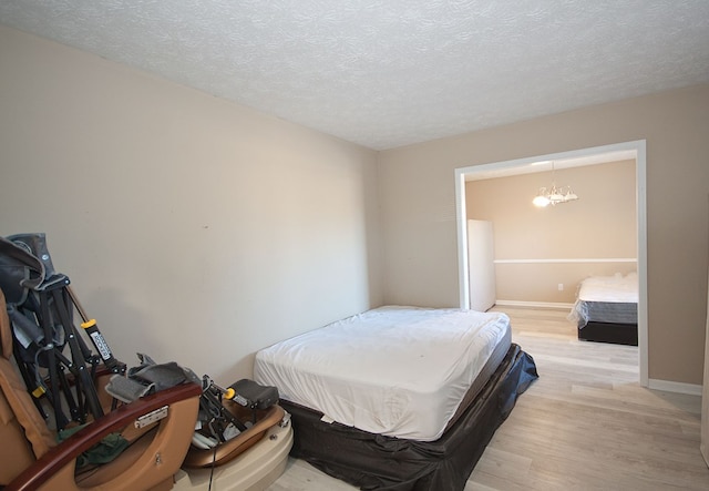 bedroom with light wood-type flooring, a chandelier, and a textured ceiling