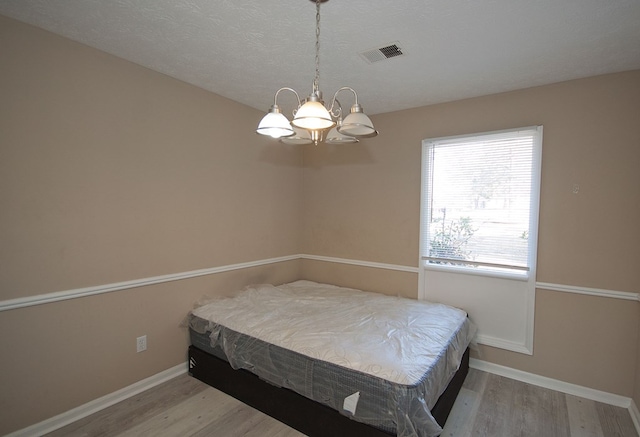 bedroom featuring wood-type flooring, a textured ceiling, and a chandelier