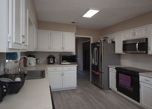 kitchen with a textured ceiling, appliances with stainless steel finishes, white cabinets, and sink