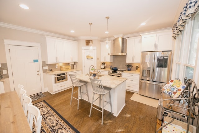 kitchen with white cabinetry, a kitchen island with sink, wall chimney range hood, and appliances with stainless steel finishes