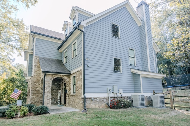 back of property featuring a lawn, central AC, and a trampoline