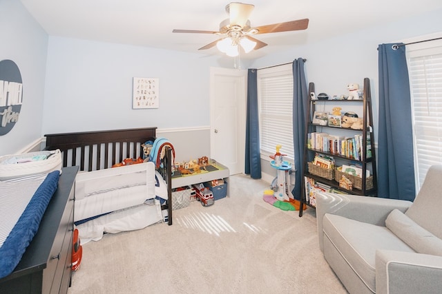 carpeted bedroom featuring a nursery area and ceiling fan