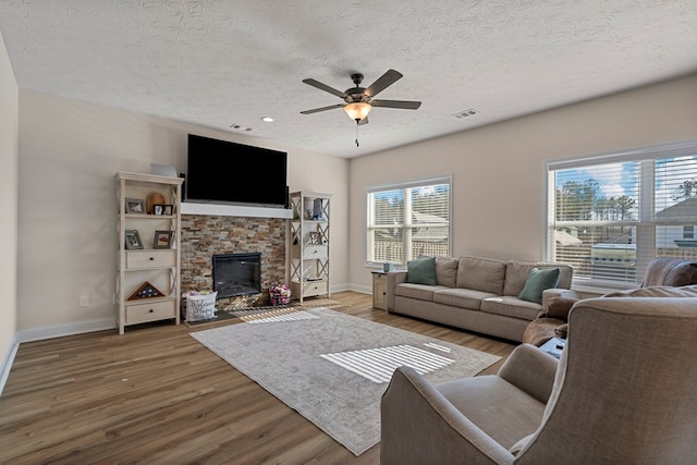 living room featuring hardwood / wood-style floors, a stone fireplace, a textured ceiling, and ceiling fan