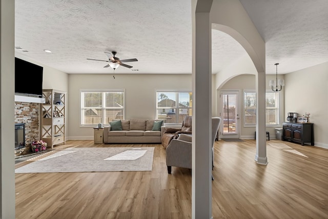 living room with ceiling fan with notable chandelier, light hardwood / wood-style floors, and a textured ceiling