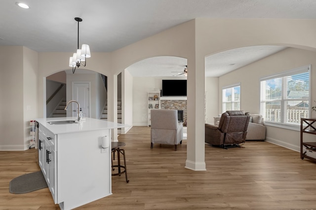 kitchen with decorative light fixtures, an island with sink, sink, white cabinets, and light wood-type flooring