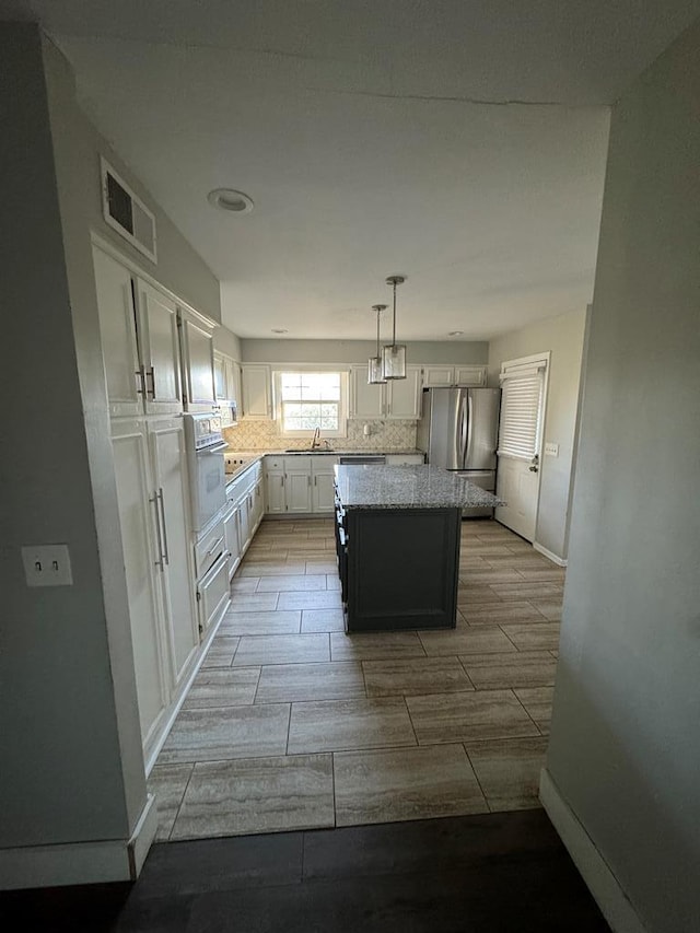 kitchen featuring hanging light fixtures, a kitchen island, stainless steel fridge, oven, and white cabinets