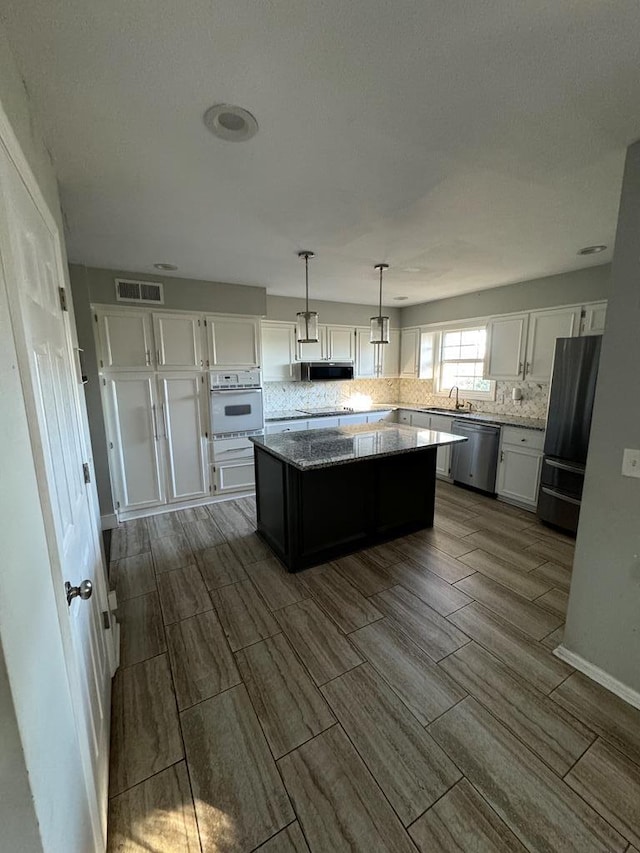 kitchen featuring sink, a center island, hanging light fixtures, white cabinets, and appliances with stainless steel finishes