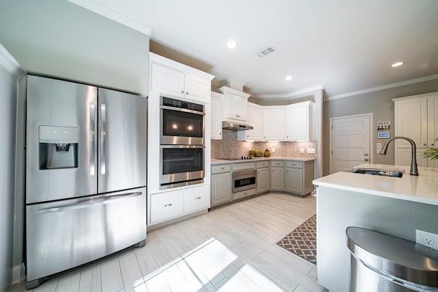 82 Rolling Meadows Way, Waverly Hall, GA 31831 - kitchen featuring stainless steel appliances, under cabinet range hood, crown molding, tasteful backsplash, and light countertops