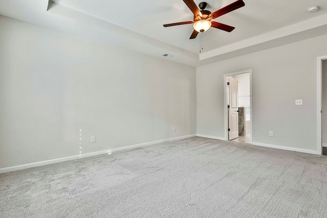 unfurnished room with ceiling fan, light carpet, and a tray ceiling