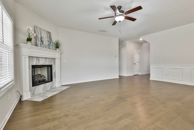 unfurnished living room with ceiling fan, a high end fireplace, and dark wood-type flooring