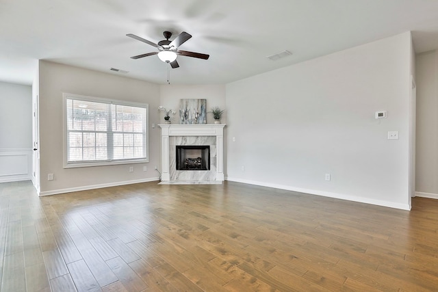 unfurnished living room featuring a high end fireplace, dark hardwood / wood-style floors, and ceiling fan