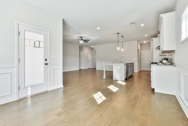 kitchen featuring hanging light fixtures, ceiling fan, an island with sink, light hardwood / wood-style floors, and white cabinetry