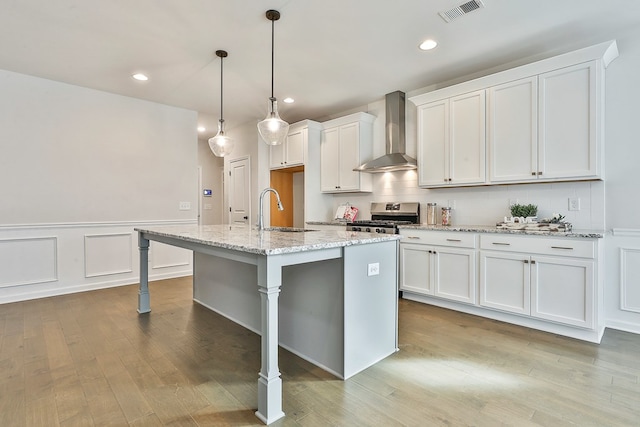 kitchen with wall chimney exhaust hood, sink, stainless steel gas stove, white cabinetry, and an island with sink