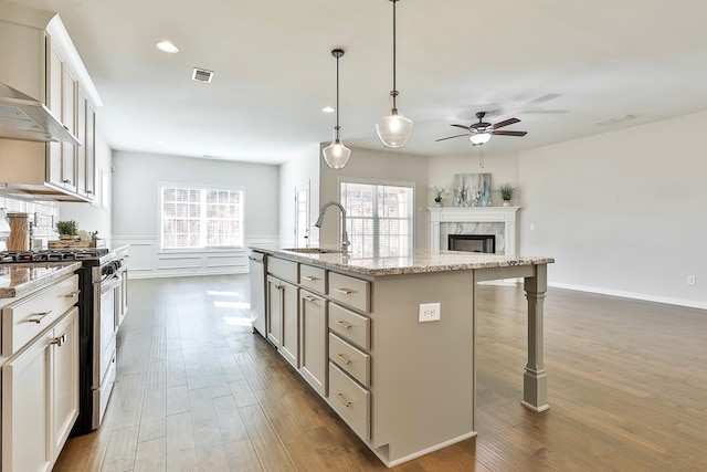 kitchen featuring appliances with stainless steel finishes, light stone counters, a kitchen island with sink, sink, and pendant lighting