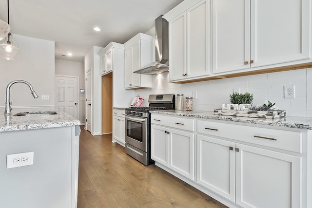 kitchen with wall chimney range hood, light hardwood / wood-style floors, decorative light fixtures, white cabinets, and stainless steel range with gas stovetop