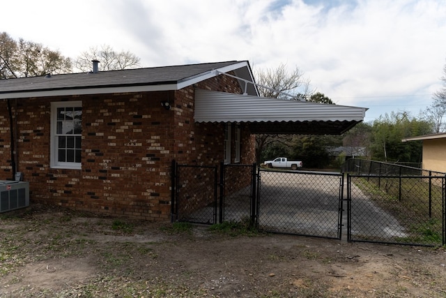 view of home's exterior with dirt driveway, central AC unit, a gate, a carport, and brick siding