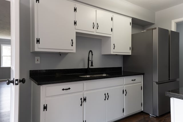 kitchen with white cabinets, dark countertops, dark wood-style floors, freestanding refrigerator, and a sink