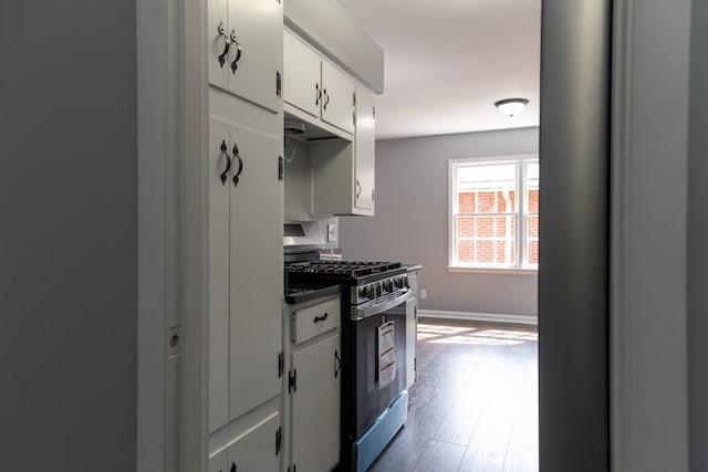 kitchen with dark wood-style flooring, dark countertops, stainless steel range with gas stovetop, white cabinetry, and baseboards