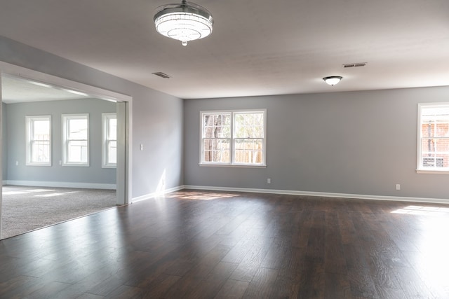 unfurnished room with dark wood-type flooring, a wealth of natural light, visible vents, and baseboards