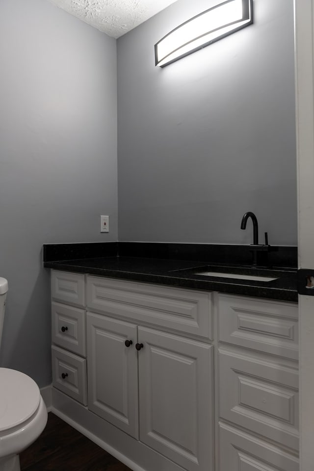 half bathroom with a textured ceiling, toilet, wood finished floors, vanity, and baseboards