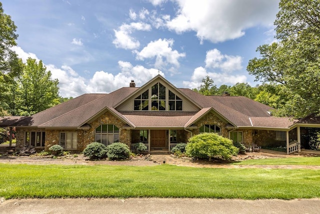 view of front of property with stone siding, a front lawn, a chimney, and a porch