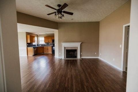 unfurnished living room featuring a fireplace with flush hearth, a textured ceiling, a ceiling fan, and dark wood-style flooring