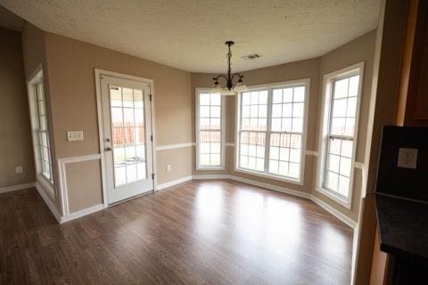 unfurnished dining area featuring a notable chandelier, a textured ceiling, visible vents, and dark wood-style flooring